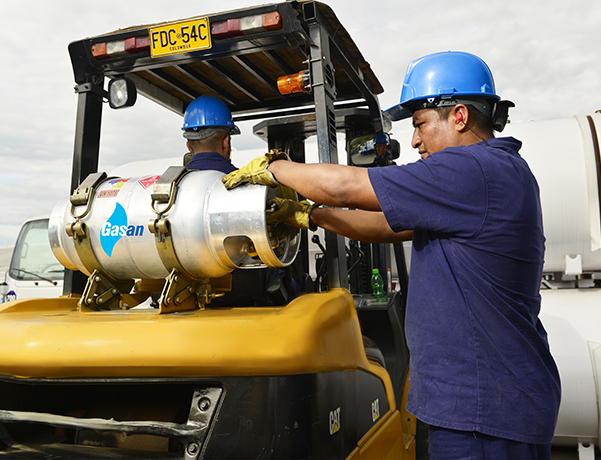 Dos hombres de uniforme azul, uno sostiene un cilindro con el logo de Norgas a un lado y otro está montado encima de un tractor